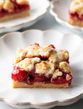 Square piece of cherry pie bar on a white scalloped plate.