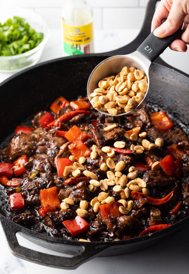 Hand is adding chopped peanuts into the skillet. 