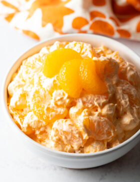 Top down view of mandarin orange fluff salad in a white bowl, garnished with 3 slices of oranges.