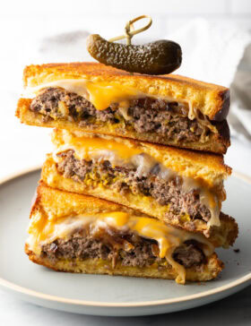 Three pieces of two patty melts stacked on top of each other. A wood skewer with small pickle is going through the top of the sandwich stack.
