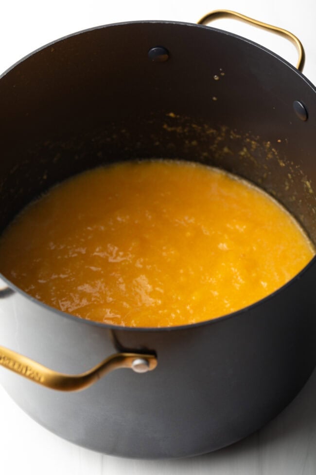 Large black cooking pot with cooked peach preserves.