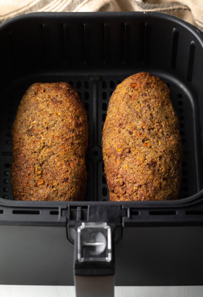 Two baked meatloaves in an air fryer basket.