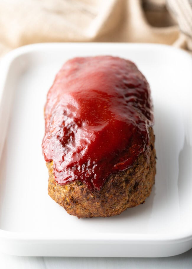Cooked meatloaf on a white plate with tomato glaze.