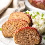 Three slices of air fryer meatloaf on a white plate, with a side of fluffy mashed potatoes and sliced scallions.