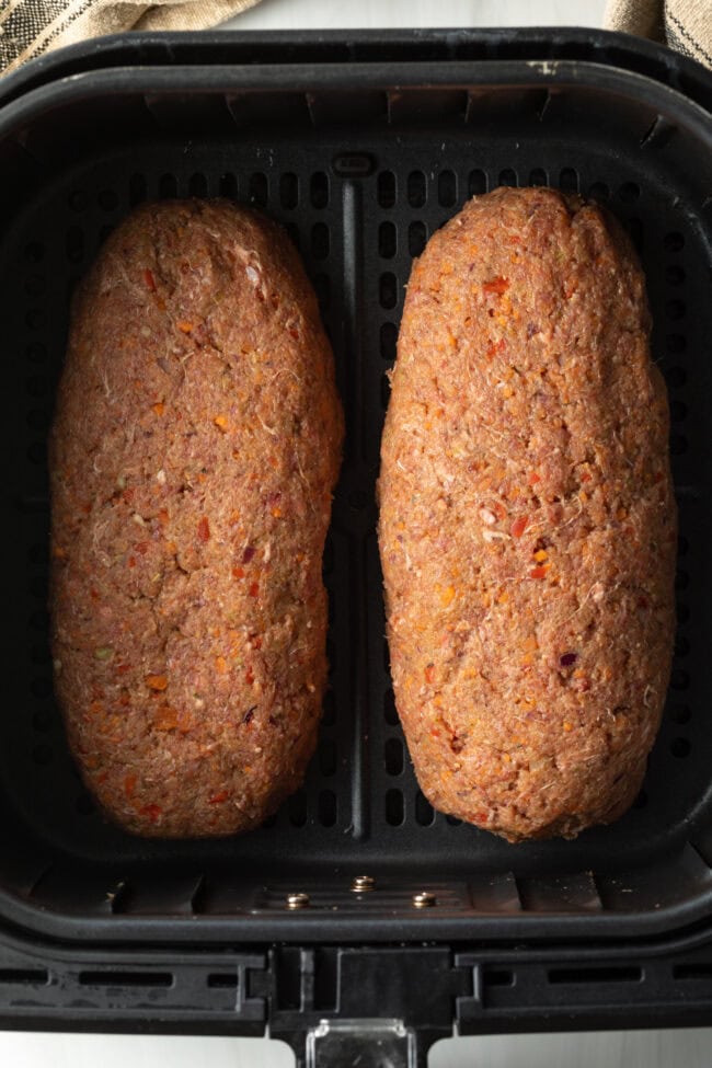 Top down view two raw meatloaves in an air fryer basket.