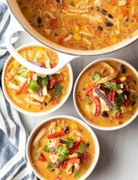 Three white and gray bowls filled with chicken taco soup. Each bowl is garnished with cilantro and red tortilla strips.