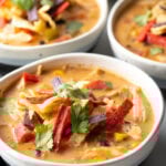 Three white and gray bowls filled with chicken taco soup. Each bowl is garnished with cilantro and red tortilla strips.