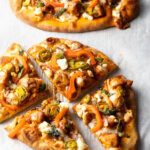 Top down 2 naan pizzas loaded with butter chicken, cheese, and veggies. One of the chicken butter masala naan pizzas is nut into 4 triangles.