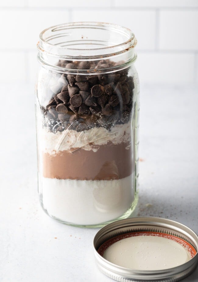 Homemade Ghirardelli brownie mix, dry ingredients layered in a large mason jar with lid off and next to the jar.