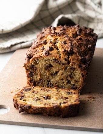 Loaf of high protein banana bread with chocolate chips. 1 slice is cut in front of the loaf.