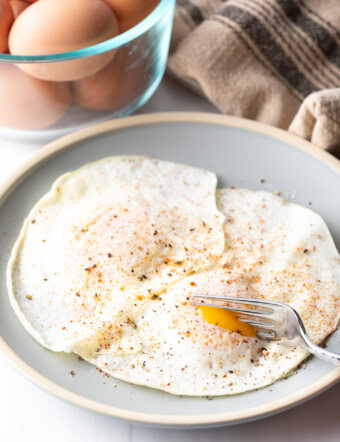 Fork cutting into th soft yolk of a gently over easy fried egg, on a light blue plate.