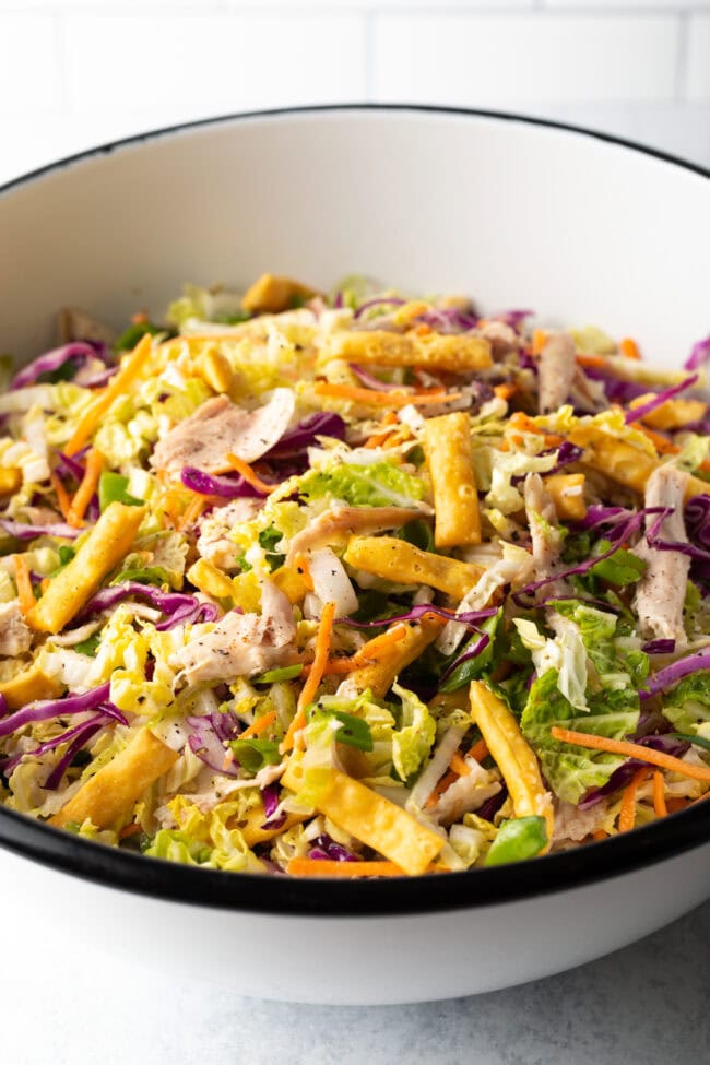 Chinese chicken salad with colorful cabbage, carrots, and crispy wontons tossed in a homemade ginger dressing in a large white bowl.