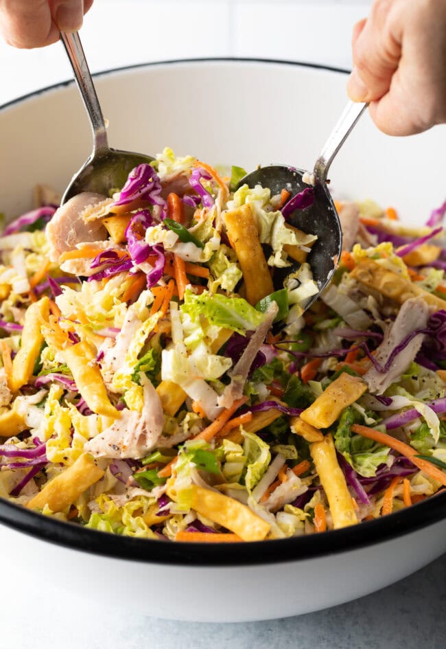 Hand with two salad forks tossing the ingredients together in the white bowl.