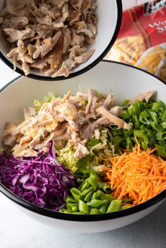 Adding cooked shredded chicken from a bowl into the salad