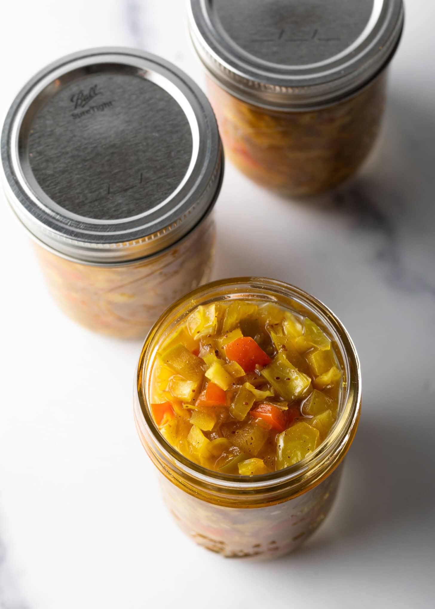 Top down view two glass jars of chowchow. One has metal lid on, the other has the lid off.