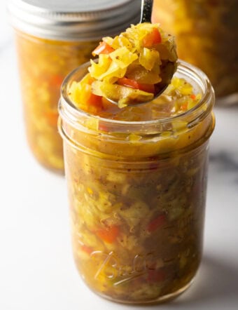 Glass jar of southern chow chow. The lid is off and to the right side, a metal spoon is in the jar showing a scoop to camera.