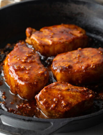 4 pork chops in a black cast iron skillet, covered in a sticky honey soy sauce.