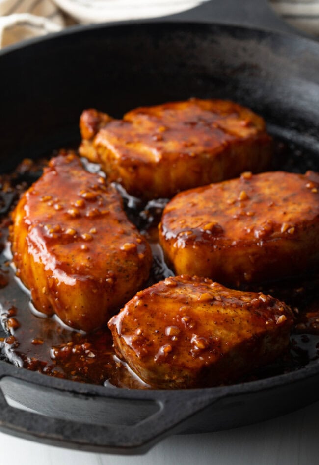 4 pork chops in a black cast iron skillet, covered in a sticky honey soy sauce.