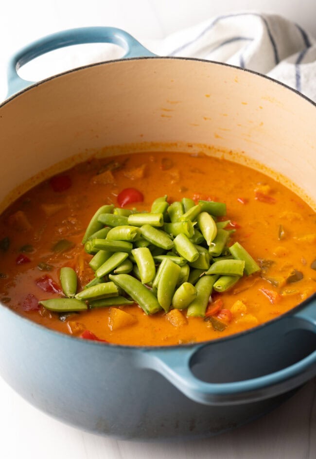 Adding fresh snap peas to the cooking pot.