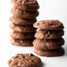 Two stacks of fudgy chocolate brownie mix cookies. One cookie in laying on the white foreground.