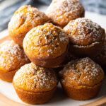 Stack of fluffy muffins made with pumpkin puree, each dusted with powdered sugar.