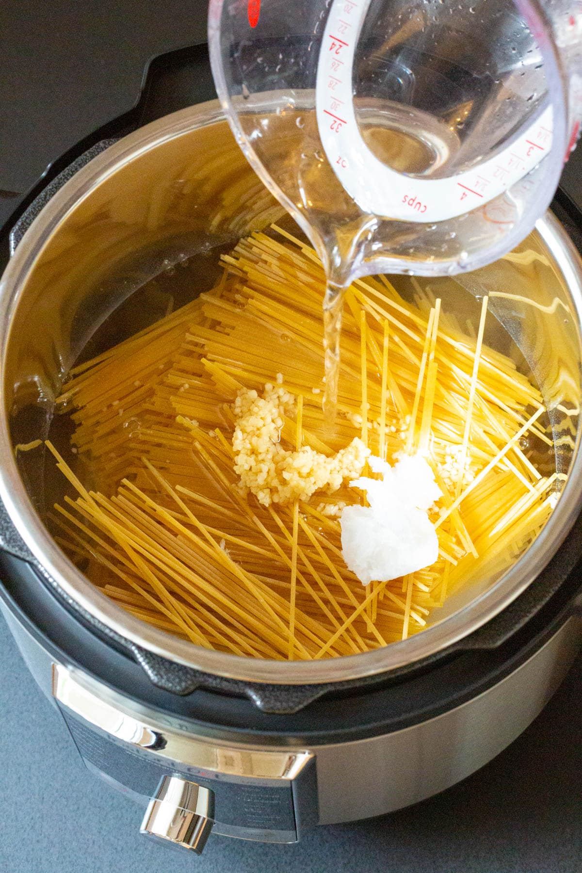 Water being poured over uncooked pasta in the Instant Pot. 