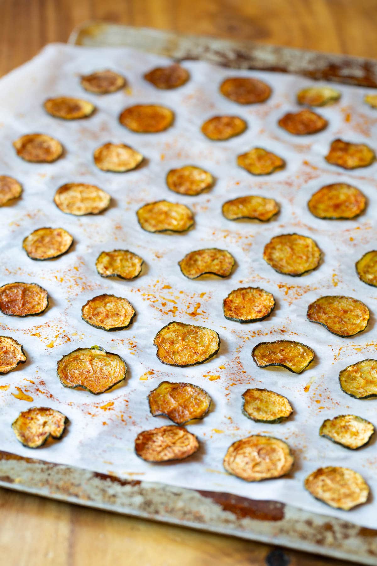 Baked Zucchini Chips #ASpicyPerspective #Healthy #Paleo #Vegan #GlutenFree #Vegetarian #ZucchiniChips #OvenRoasted Oven Baked Zucchini Chips on cookie sheet with parchment paper