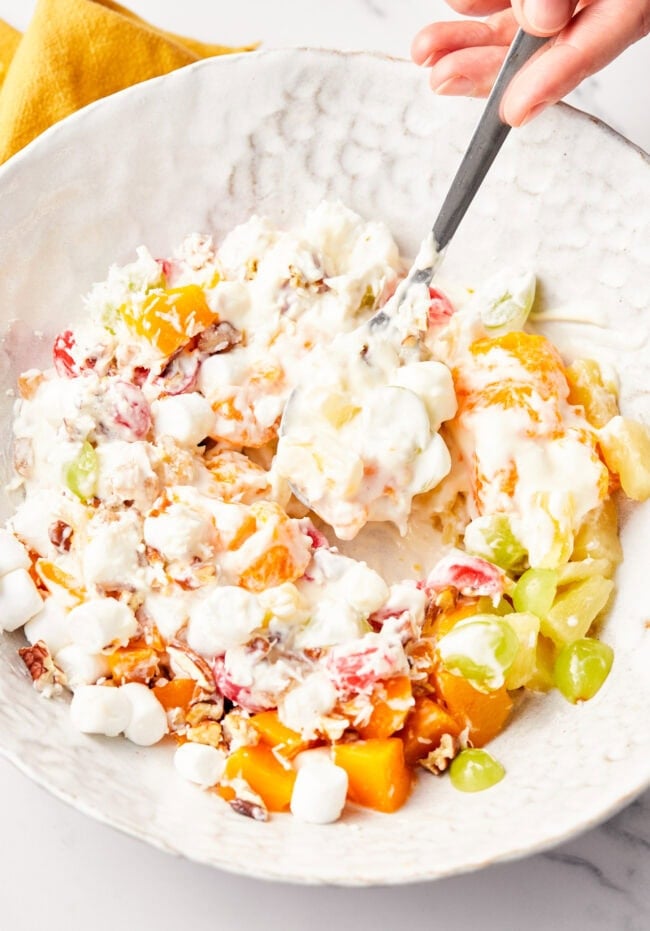 Overhead view of a spoon mixing together the ambrosia salad in a mixing bowl. 