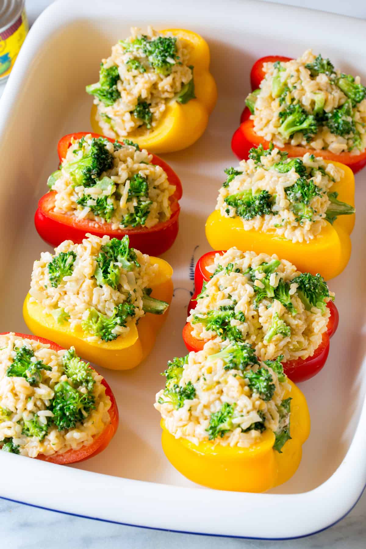 Uncooked bell peppers in a roasting dish stuffed with a mixture of cooked rice and broccoli.