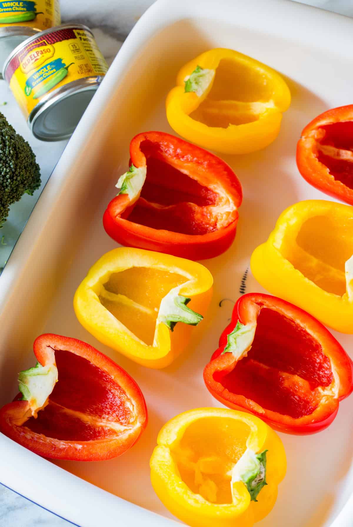 Halved red and yellow bell peppers in a white roasting dish, cut-side up.