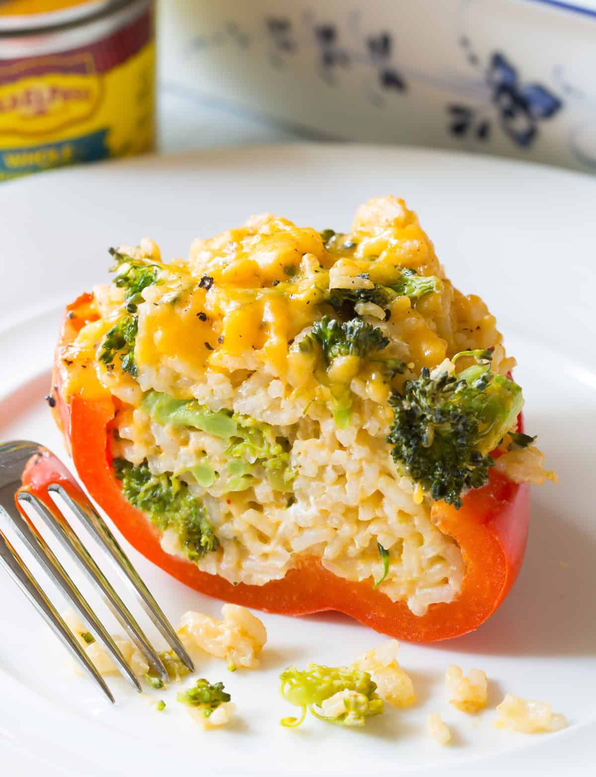 A stuffed bell pepper is halved on a white plate to show the white rice and cheesy broccoli filling.