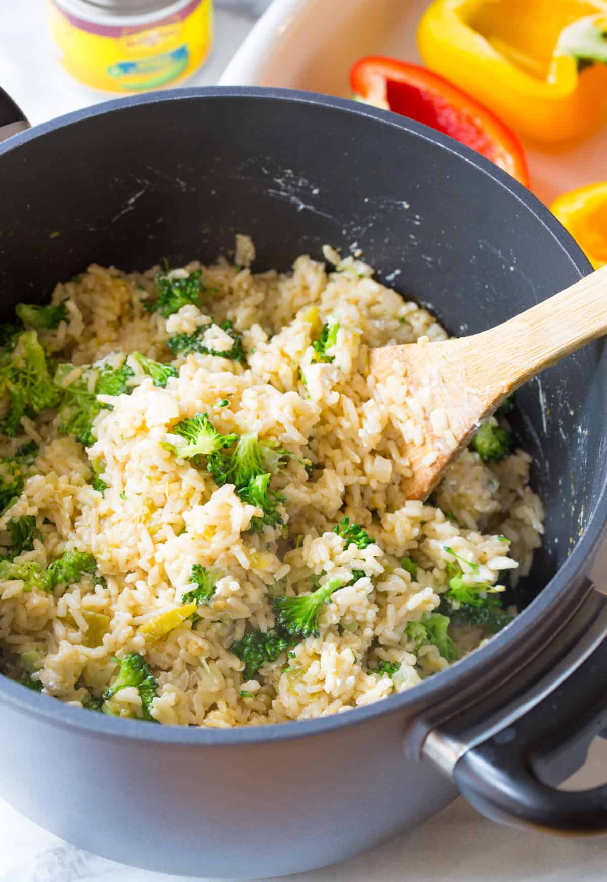 A wooden spoon stirring cooked rice and broccoli in a large cooking pot.