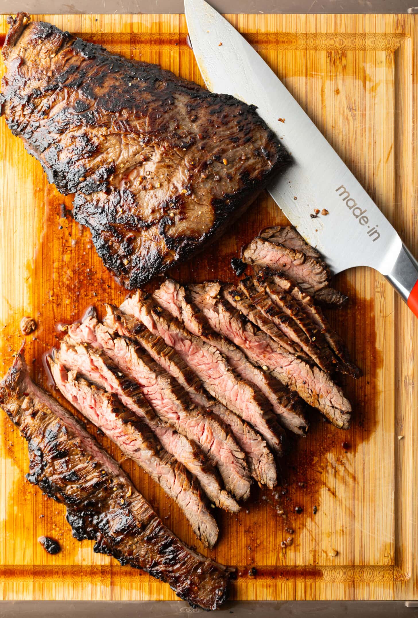 Seared steak sliced into thin strips on a wood cutting board, large knife to the side.