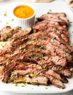 Thin slices of Bavette steak on a white serving platter with a ramekin of cowboy butter to the side.