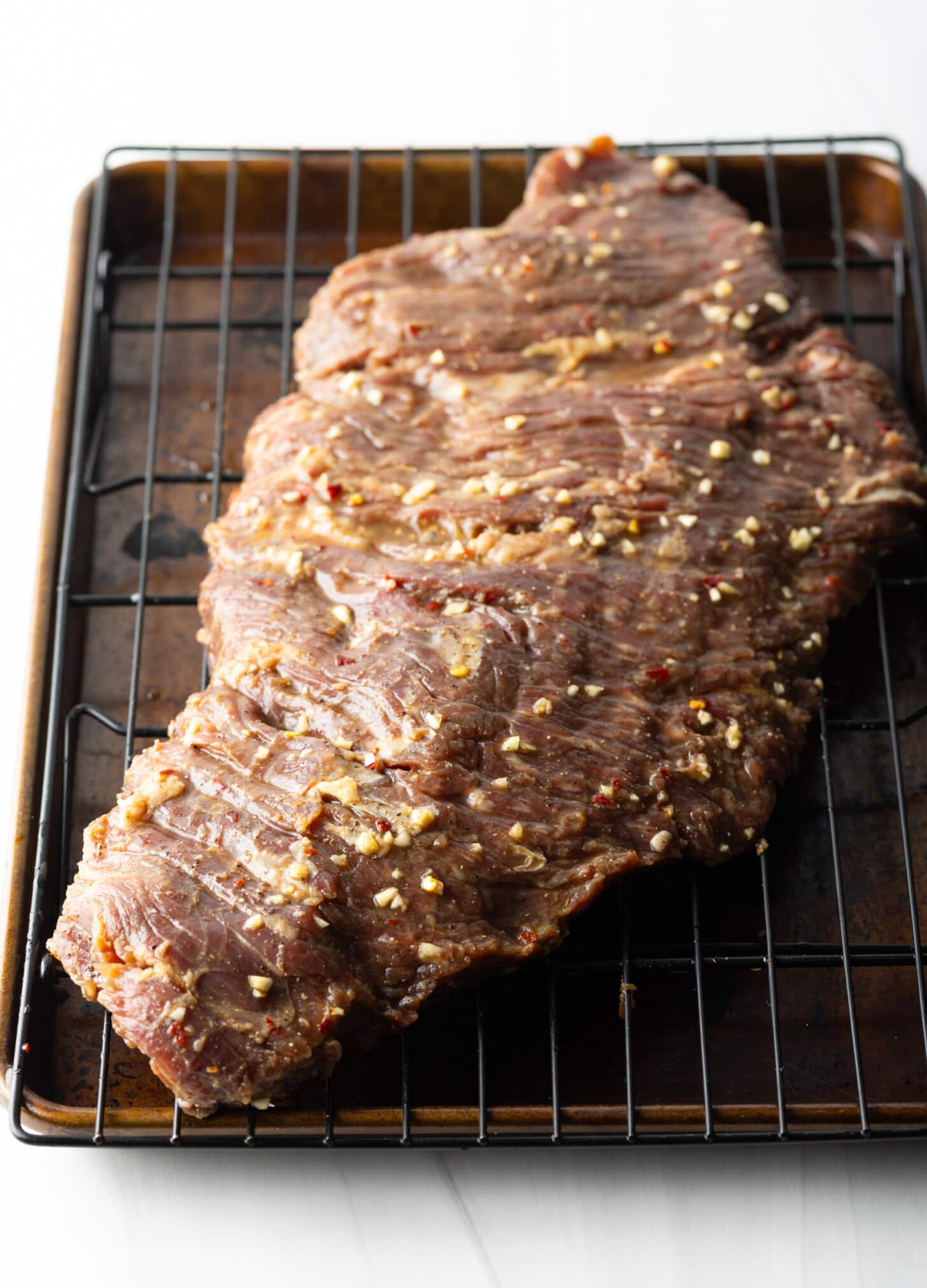 Raw large section of marinated beef on a wire rack.