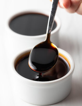 Two white ramekins of sauce. One closest to camera has a metal spoon with a spoonful showing to camera.