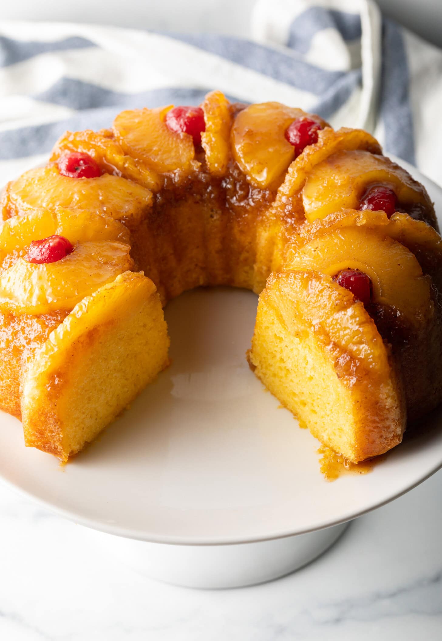 Upside down pineapple cake on a white cake stand. The cake has a large section removed, showing the tender yellow inside of the cake.