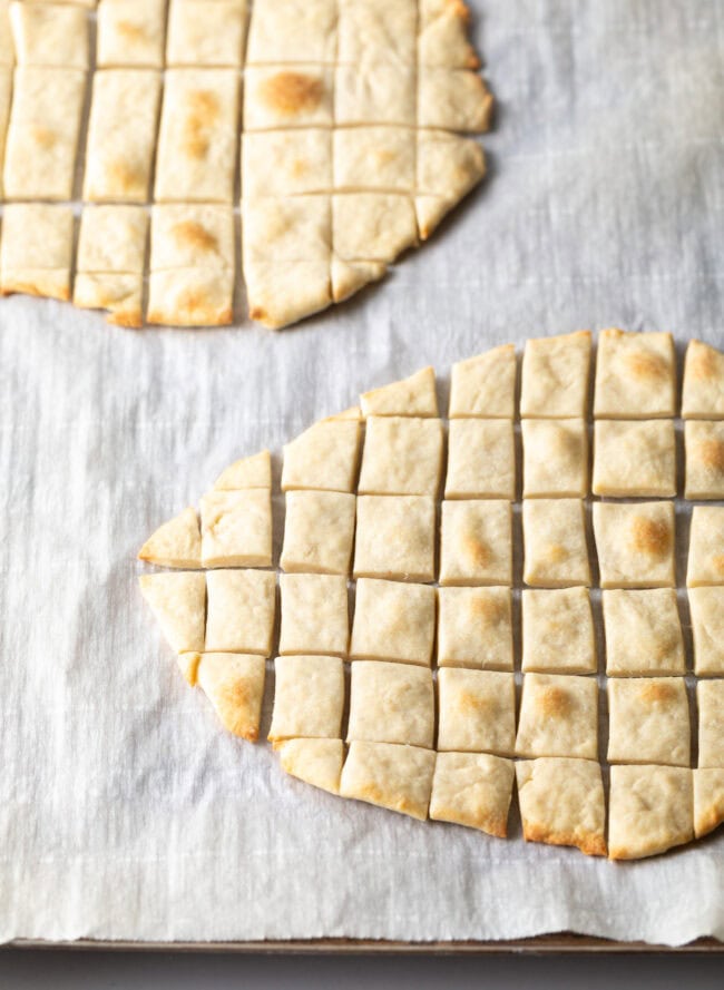Two pieces of unleavened bread laying on a gray background. Each large oval of bread has been sliced into small squares.