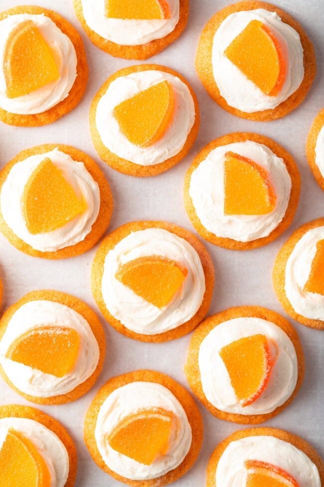 Top down view of several sugar orange cookies with white frosting and candy orange slice.