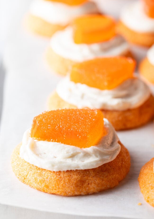 Close view of half a dozen orange sugar cookies topped with frosting and a candy orange slice.