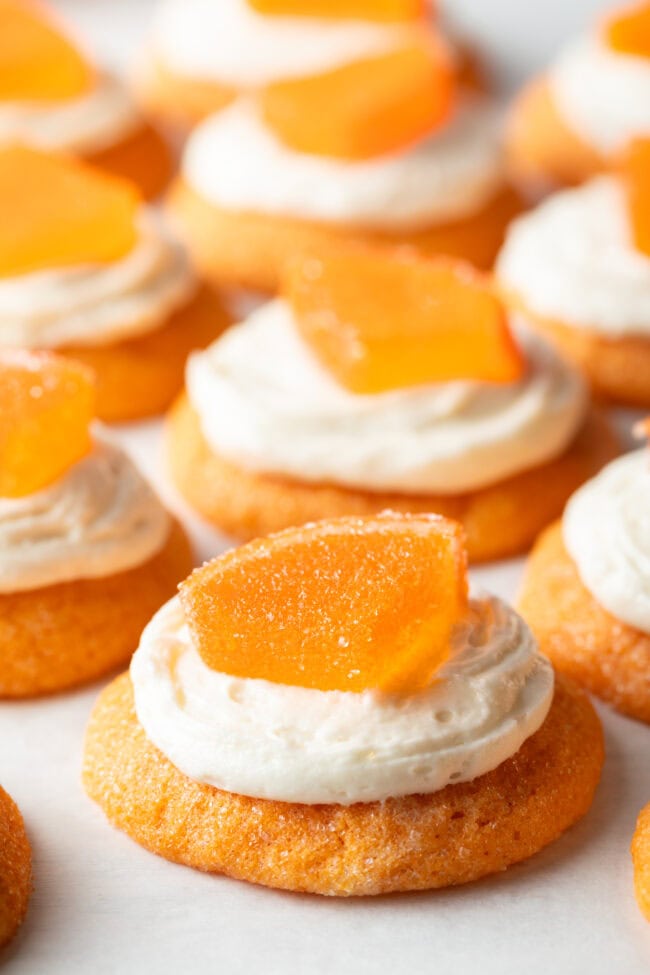 Close view of half a dozen orange sugar cookies topped with frosting and a candy orange slice.