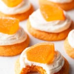 Several sugar orange cookies with white frosting and candy orange slice. One cookie has a bite taken out of it.