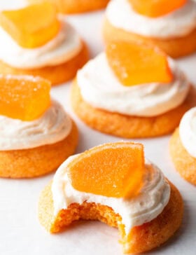 Several sugar orange cookies with white frosting and candy orange slice. One cookie has a bite taken out of it.