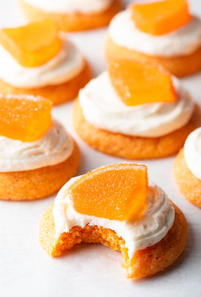 Several sugar orange cookies with white frosting and candy orange slice. One cookie has a bite taken out of it.