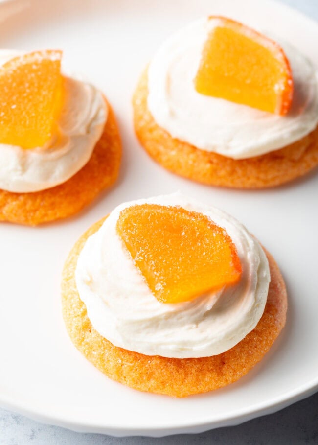 Close view of 3 orange sugar cookies topped with frosting and a candy orange slice.