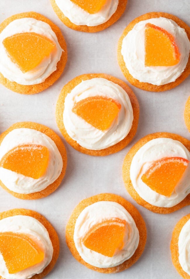 Top down view of several sugar orange cookies with white frosting and candy orange slice.