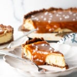 Slice of salted caramel cheesecake on a white plate with a fork.