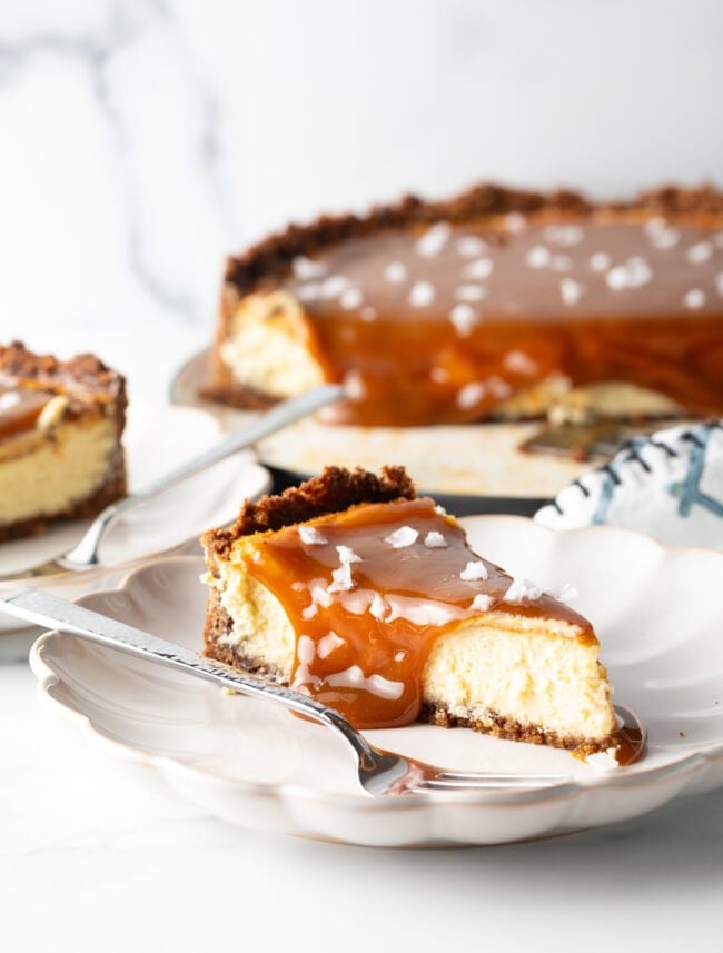 Slice of salted caramel cheesecake on a white plate with a fork.