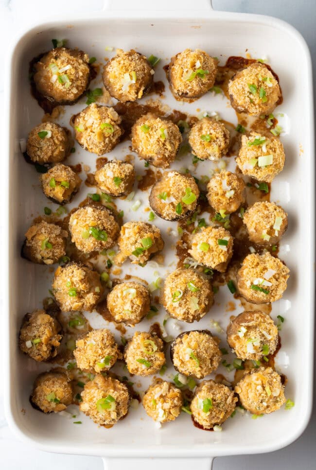 Top down view, two dozen seafood stuffed mushrooms with ritz crackers in a white baking dish.