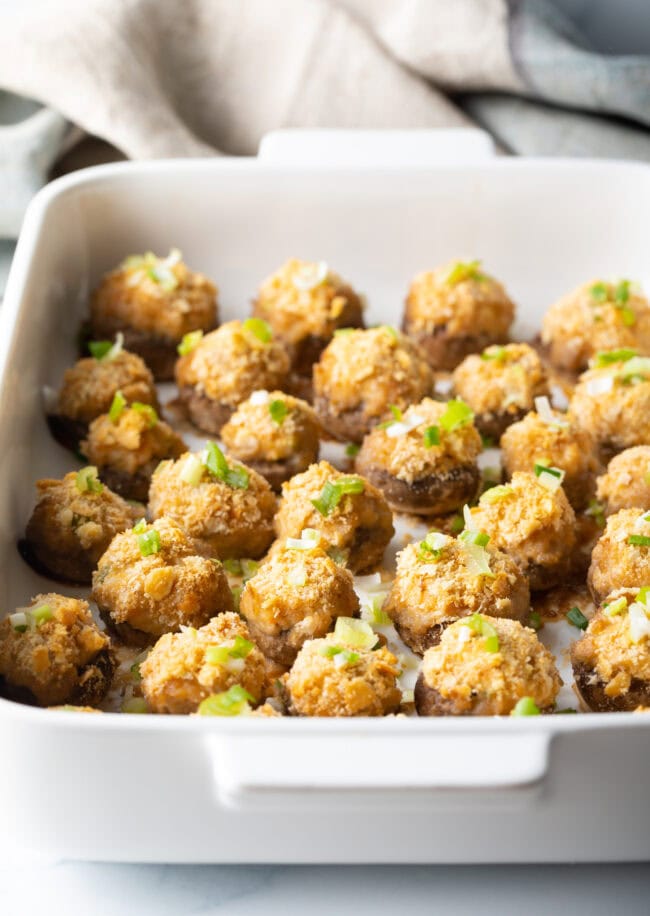 Two dozen crab stuffed mushrooms with ritz crackers in a white baking dish.
